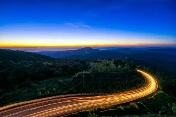 Photo of Sunrise scence of car light trail to the top with curve of road at Doi Inthanon National park in Chiang Mai Province, Thailand.