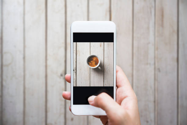 Hand photographing coffee mug on white wooden table with smart phone