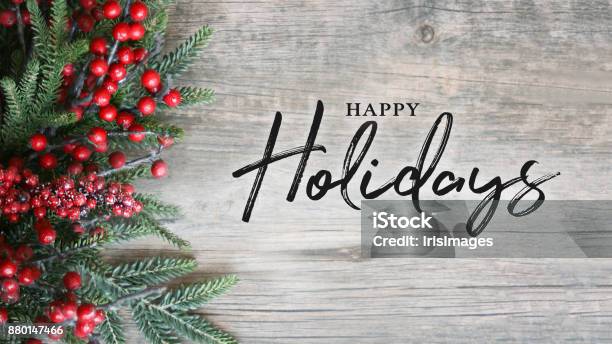 Happy Holidays Text With Holiday Evergreen Branches And Berries Over Rustic Wooden Background Stock Photo - Download Image Now