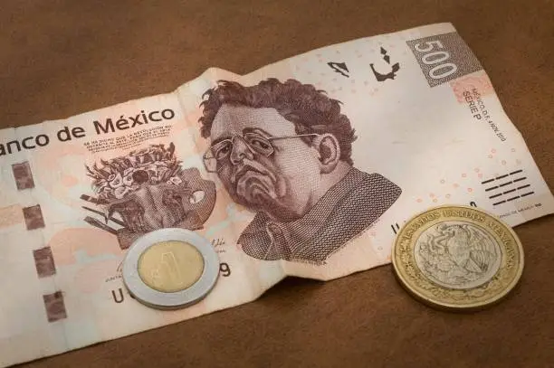 A 500 mexican pesos bill seems to be sad. A coin of 1 peso and the back of one of 10 are also show.
