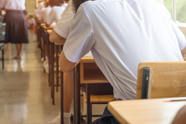 istock Asian School students in uniform taking examination , writing answer sheet in classroom, educational school, view of boys having exams in class on seat rows, Education system tests concept of Thailand 880205408