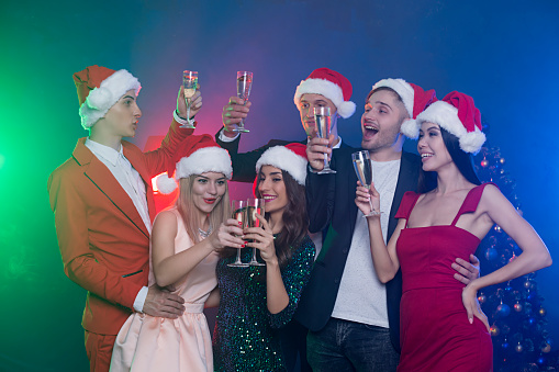 A party with friends. Cheerful group of friends in santa hats posing with champagne at New Year's or Christmas party.