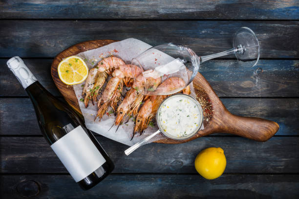 riesengarnelen oder scampi mit weißer soße, flasche wein, glas für den wein und einer halben zitrone auf einem holzbrett. ansicht von oben - prepared shrimp prawn large grilled stock-fotos und bilder