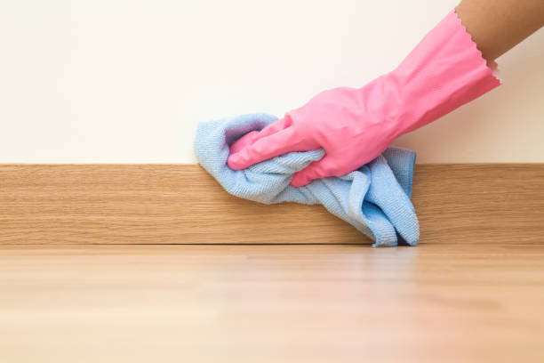 Employee hand in rubber protective glove with micro fiber cloth wiping a baseboard on the floor from dust at the wall. Spring general or regular clean up. Commercial cleaning company concept. stock photo