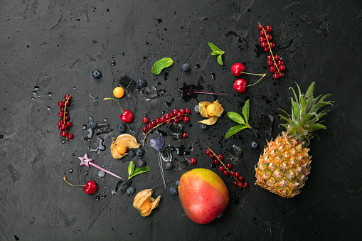 <<Group of fresh juisy blueberries - mango, pineapple, red currant, blueberry, mint, cherry, cherry, physalis, and ice cubes on black background. Top view with copy space. Healthy Food Backgrounds>>