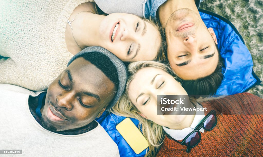 Top view of multiracial best friends having fun resting together outdoors on sunny day - Happy friendship and peace concept with young multicultural people on relax mood - Bright vintage filtered look Friendship Stock Photo