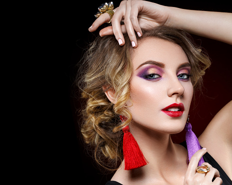 beautiful blond young woman with bright purple makeup and tassel earrrings. studio beauty shot on black background. copy space.
