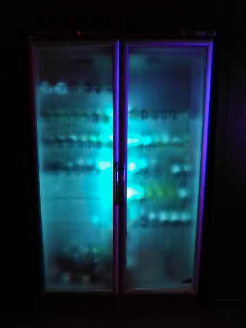 Glowing iced cold beverage bottle fridge in darkness