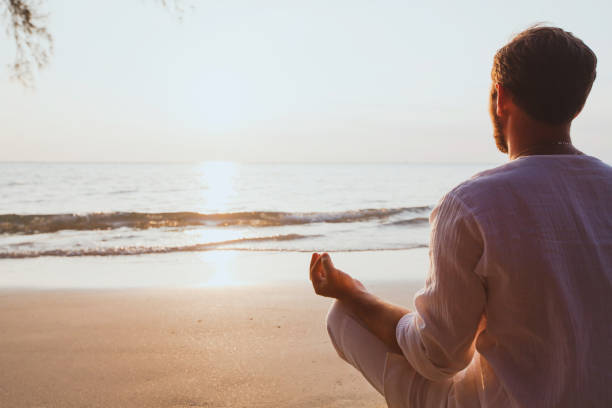 istock meditation, man practicing yoga at sunset beach 880404694