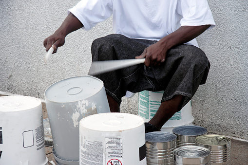 Young African American man beating out the rhythm on plastic container bucket drums. Horizontal.