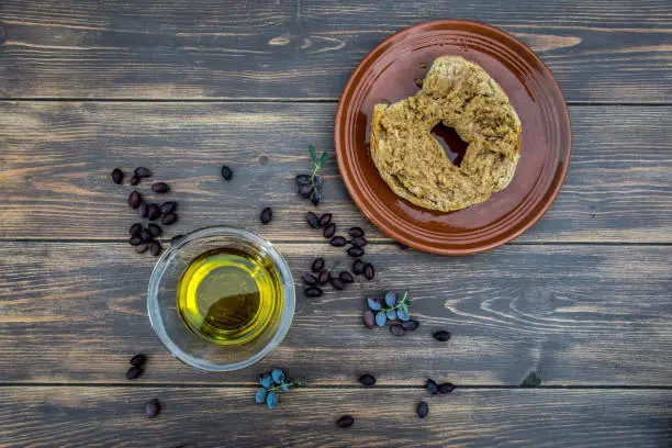 Bowl with extra virgin olive oil, olives, a fresh branch of olive tree and cretan rusk dakos close up on wooden table, Crete, Greece.