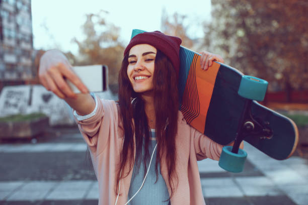 istock Young woman is holding a longboard and doing selfie 880486006