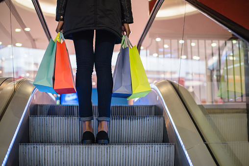 Piernas de mujer con bolsas coloridas en la escalera mecánica en un centro comercial photo