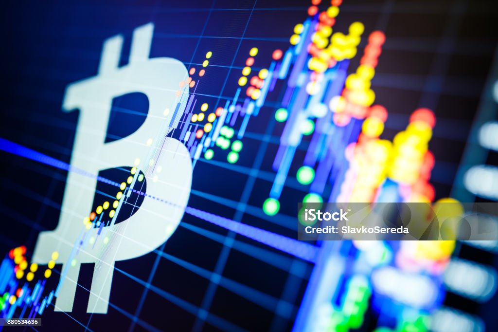 Data analyzing in exchange stock market: the candle chars on display. Analytics price change cryptocurrency BTC to USD (Bitcoin / US Dollar), the most popular pair in the world. Big Bitcoin logo. Bitcoin Stock Photo