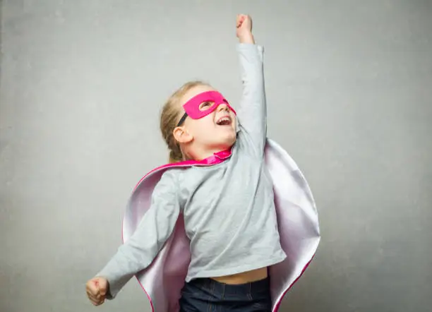 Photo of Little girl pretending that she is flying wearing a cloak and mask