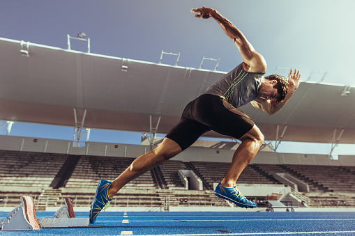 Rear view of sportsman running fast at the beach at sunrise or sunset. Athlete training outdoors with copy space. Sport motivation concept