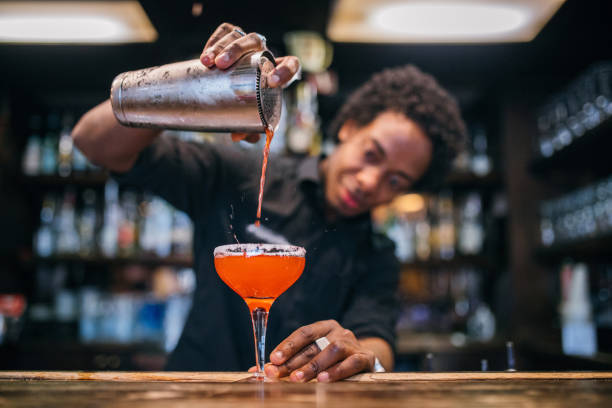 junge barkeeper cocktails in einer cocktailbar gießen - cocktailshaker stock-fotos und bilder