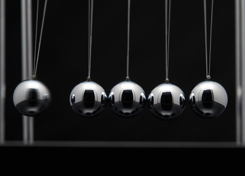 Newton's cradle office toy. Studio shot of swinging metal balls on black background.