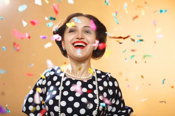 Happy girl on yellow background, colorful confetti slowly scatter and fall