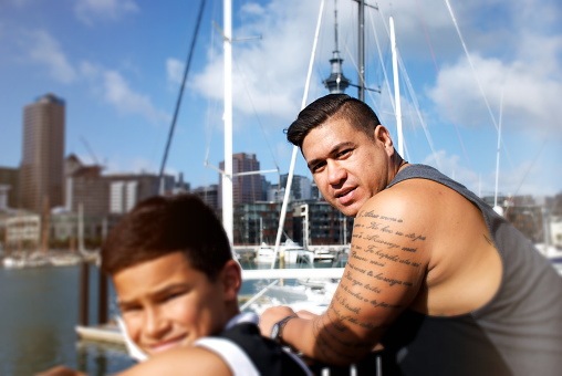 Focus on a Pacific Islander Father with his Son Looking to Camera against a Urban Cityscape Marina Scene.