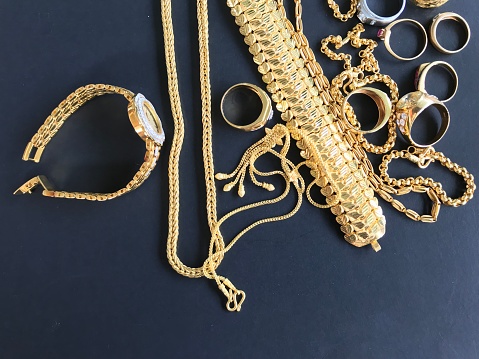 Pile of golden necklace, bracelet and rings on black background