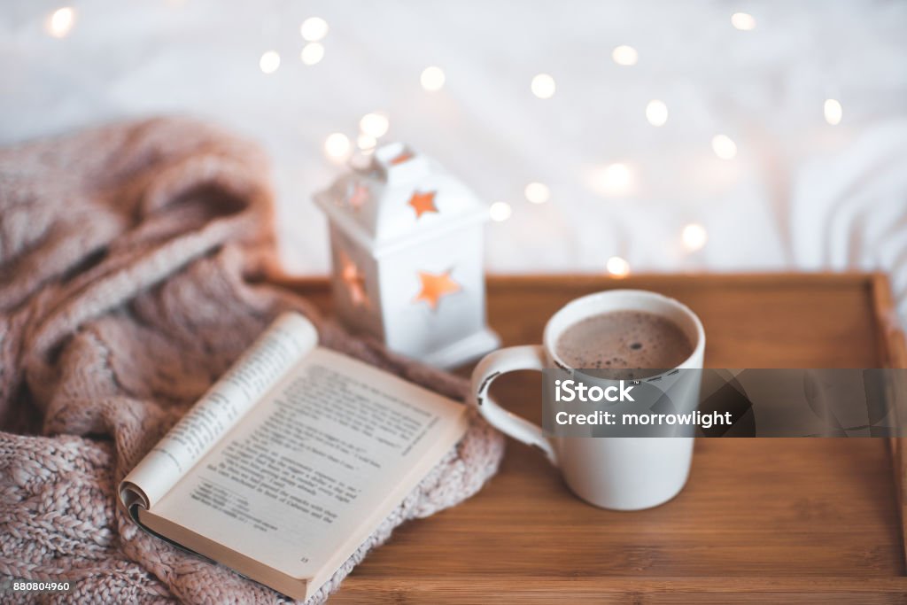 Christmas cup of coffee Good morning. Cup of coffee ith opn boon on wooden tray closeup over Christmas lights. Book Stock Photo
