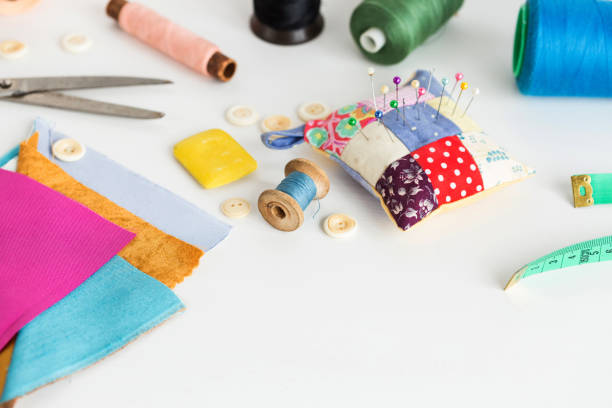 istock sewing tools, patchwork, tailoring and fashion concept - closeup on white work desk in studio, pincushion, thread spools, measuring meter, buttons, scissors, soap, pieces of colored patchwork fabric 880847928