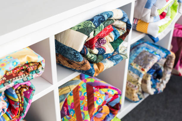 patchwork, sewing and fashion concept - colorful finished quilts in the studio at white shelves with few storage compartments, the warehouse of finished products, side view, selective focus stock photo