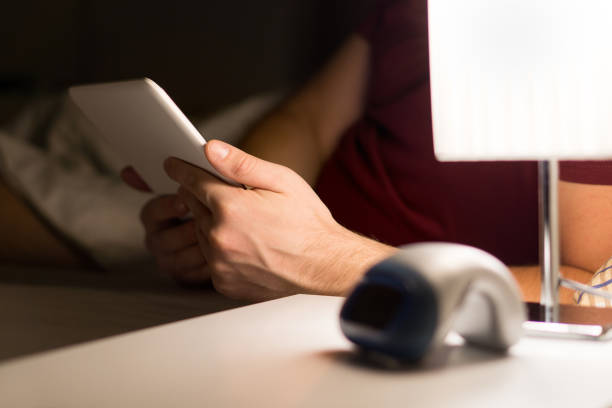 Man reading electronic book or using tablet in bed. Modern mobile device in hand in bedroom. Watching movies or series online before going to sleep.