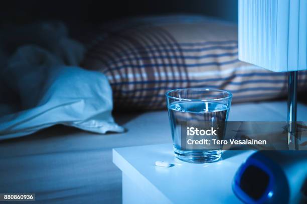 Sleeping Pill On Nightstand Next To A Glass Of Water White Tablet On Table And Bed In Bedroom Stock Photo - Download Image Now