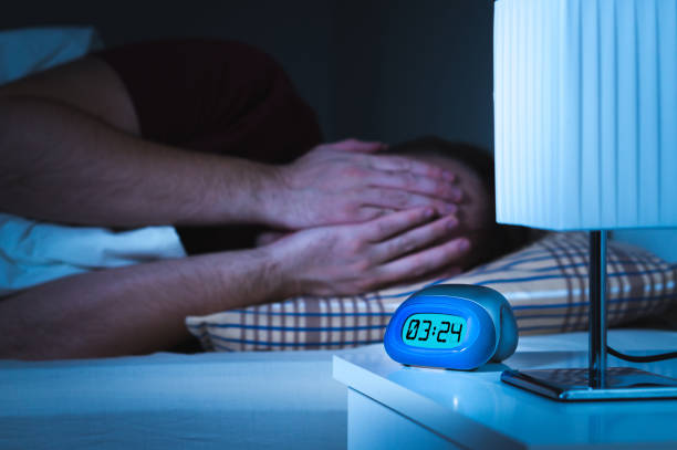 Seeing nightmares or bad dreams concept. Scared man covering face with hands in bed. Seeing nightmares or bad dreams concept. Scared man covering face with hands in bed. Alarm clock on nightstand in bedroom. mare stock pictures, royalty-free photos & images