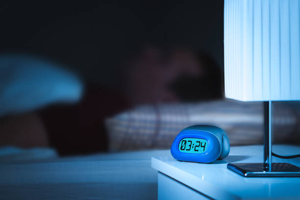 Man sleeping in bed. Digital alarm clock on nightstand in bedroom.