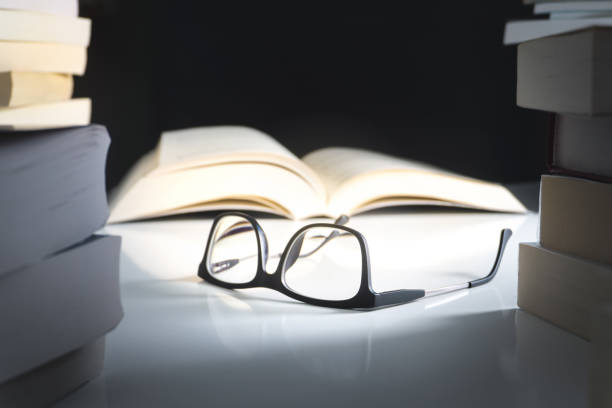 Glasses and open book on table surrounded by literature. Education, learning and reading concept.