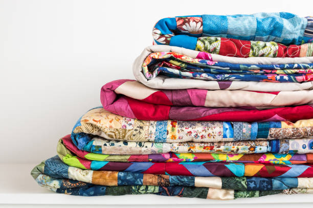 sewing, patchwork and fashion concept - beautiful colorful quilts were neatly folded and stored in several rows in height for storage, sale of finished textile stitched products on white background stock photo
