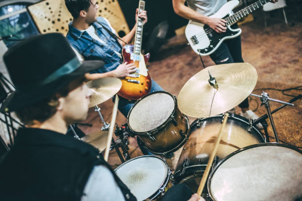 Music band repetition. Repetition of rock music band. Cropped image of bass guitar player, electro guitar player and drummer behind the drum set. Rehearsal base young man wink stock pictures, royalty-free photos & images