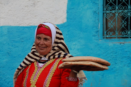 Chefchaouen, Morocco - October 30, 2016: Woman dressed in typical moroccan attire selling bread on a street in Chefchaouen, Morocco