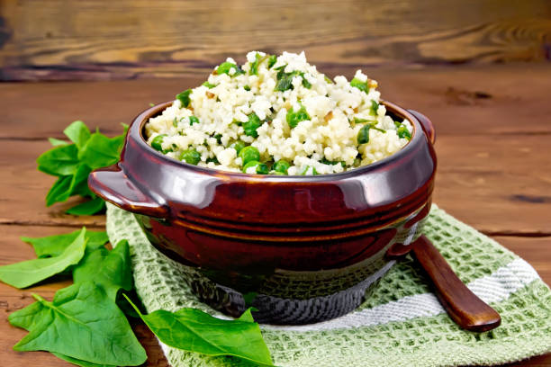 Couscous with spinach and green peas in bowl on wooden board