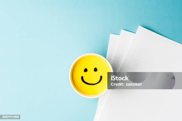 Gelbe Lächelndes Gesicht Gute Laune Pappbecher Und Papiere Auf Blauem Hintergrund Stockfoto und mehr Bilder von Wohlbefinden