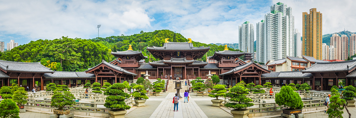 Panoramic view across the ornamental courtyard of Chi Lin as tourists photograph the traditional wooden pagoda temple overlooked by modern high rise apartment buildings in Kowloon, Hong Kong, China.