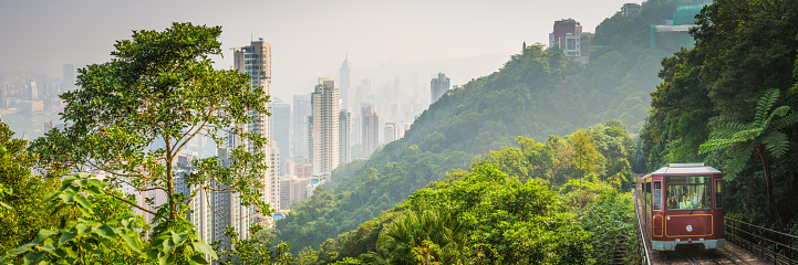 The iconic ruby cable cars of the Peak Tram climbing through  the green forests of Victoria Peak above the crowded skyscraper cityscape of Hong Kong, China.