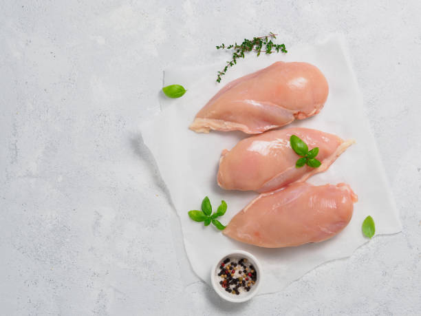 istock Raw chicken breast with fresh basil on paper over gray cement background 880966810