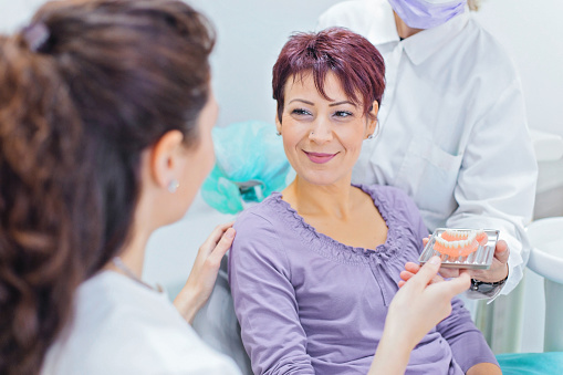 Female dentist talking to a patient and showing her teeth dentures