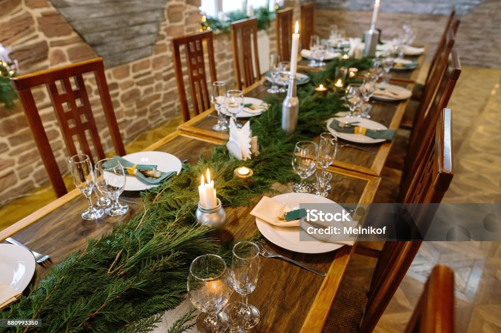 winter, atmosphere, celebration concept. in the dining room there is an elegant furniture made of natural materials, long table served and decorated with branches of spruce and candles Winter Stock Photo