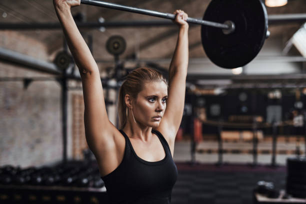istock Young woman lifting weights over her head in a gym 881003676