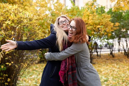 two young friend women to get together and hug each other with a big smile and joyful mood on a background of autumn Park and orange leaves