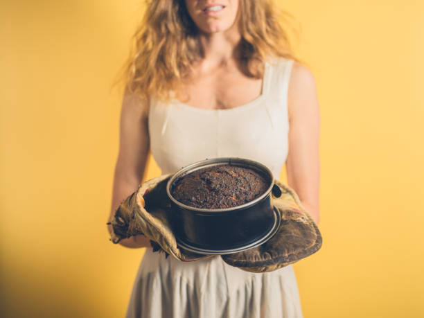 jeune femme tenant un gâteau brûlé - cooking fail photos et images de collection
