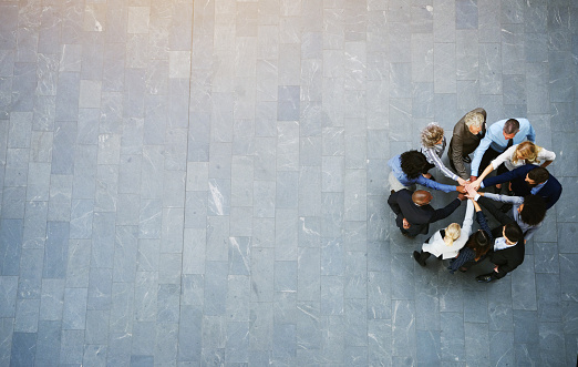 High angle view of a team of united businesspeople standing with their hands together in a huddle in the lobby of a modern office building