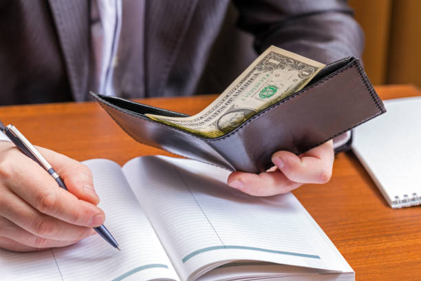 istock Businessman holding a wallet with dollars and makes entries in the diary 881068270