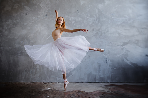 Young and slim ballet dancer is posing in stylish studio with big windows