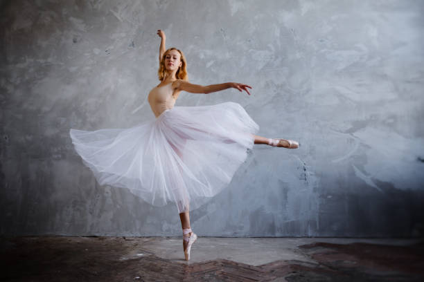 นักเต้นบัลเล่ต์หนุ่มและผอมเพรียวกําลังโพสท่าในสตูดิโอที่มีสไตล์พร้อมหน้าต่างบานใหญ่ - ballet dancer ภาพสต็อก ภาพถ่ายและรูปภาพปลอดค่าลิขสิทธิ์
